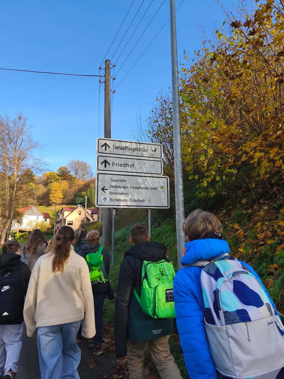 Schülerinnen und Schüler der Klasse 6c gehen bei sonnigem Wetter einen Weg entlang. Ein Wegweiser zeigt den Richtungspfeil zur Tierauffangstation Schmalkalden.