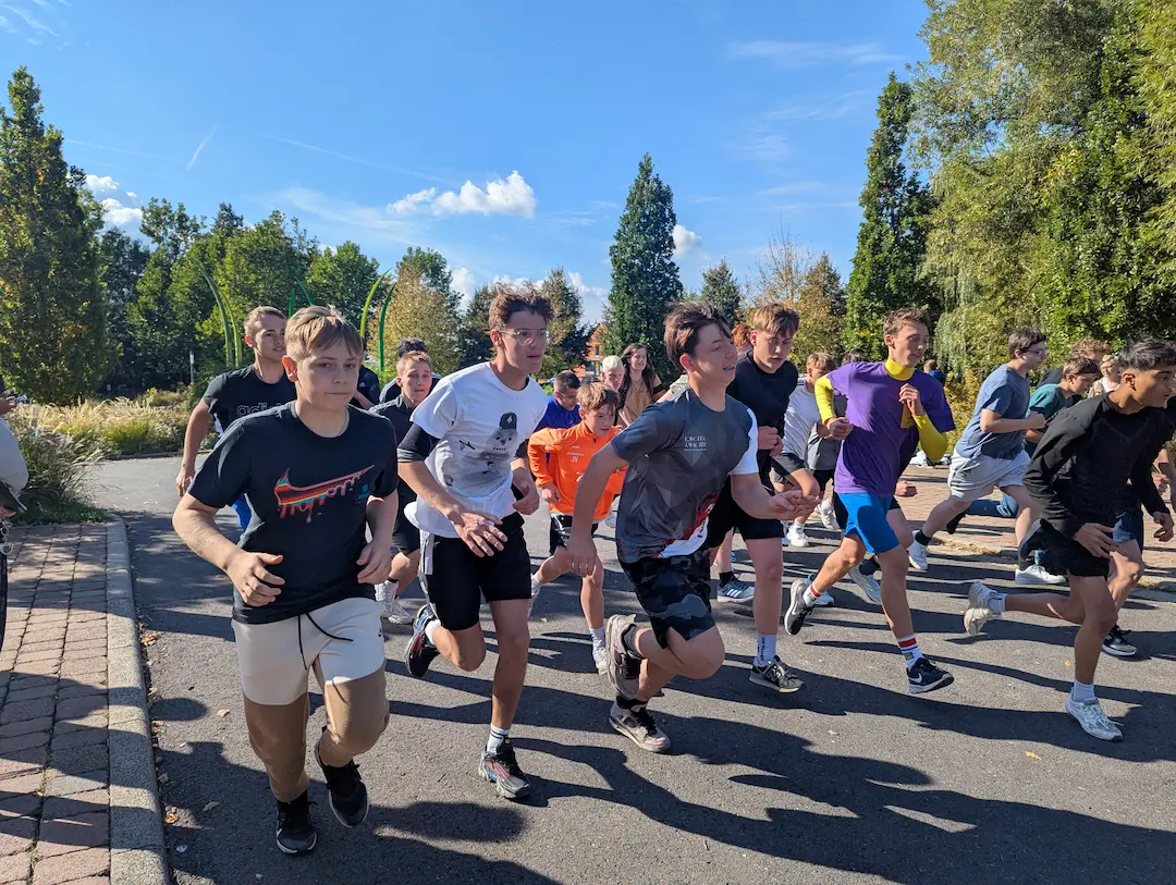 Eine Gruppe Jugendlicher startet bei einem 800-Meter-Lauf im Freien. Die Sonne scheint, und die Teilnehmenden rennen energisch los, während Zuschauer im Hintergrund zusehen.