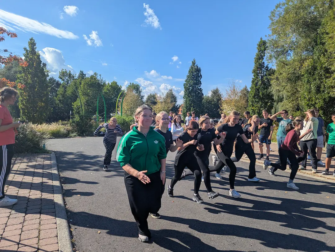 Eine Gruppe Mädchen startet motiviert zum 800-Meter-Lauf bei sonnigem Wetter. Zuschauer und andere Teilnehmende stehen am Rand und feuern sie an.