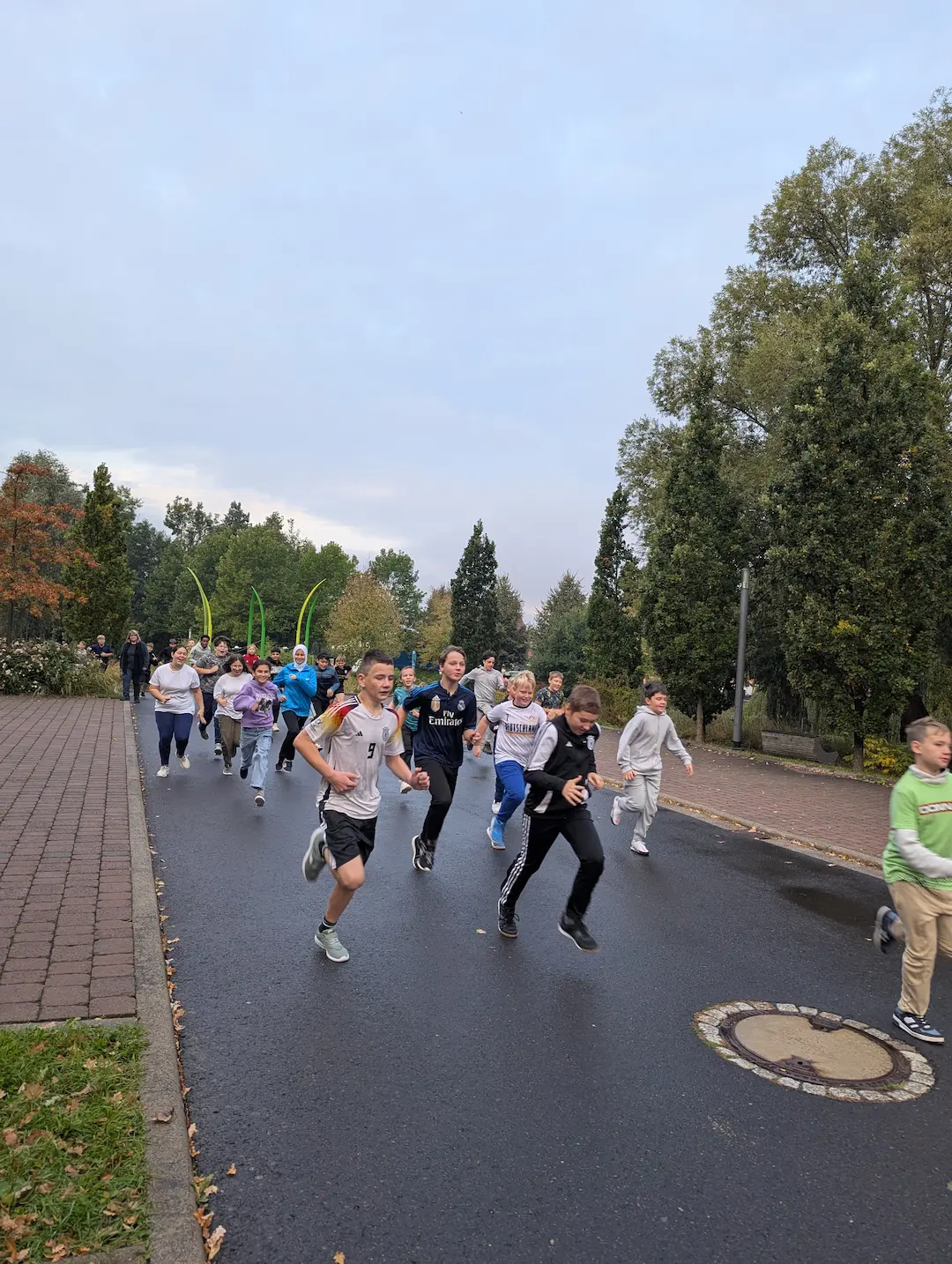 Schülerinnen und Schüler laufen in sportlicher Kleidung auf einer nassen Straße, um sich für den Wettkampf aufzuwärmen. Im Hintergrund sind herbstliche Bäume zu sehen.
